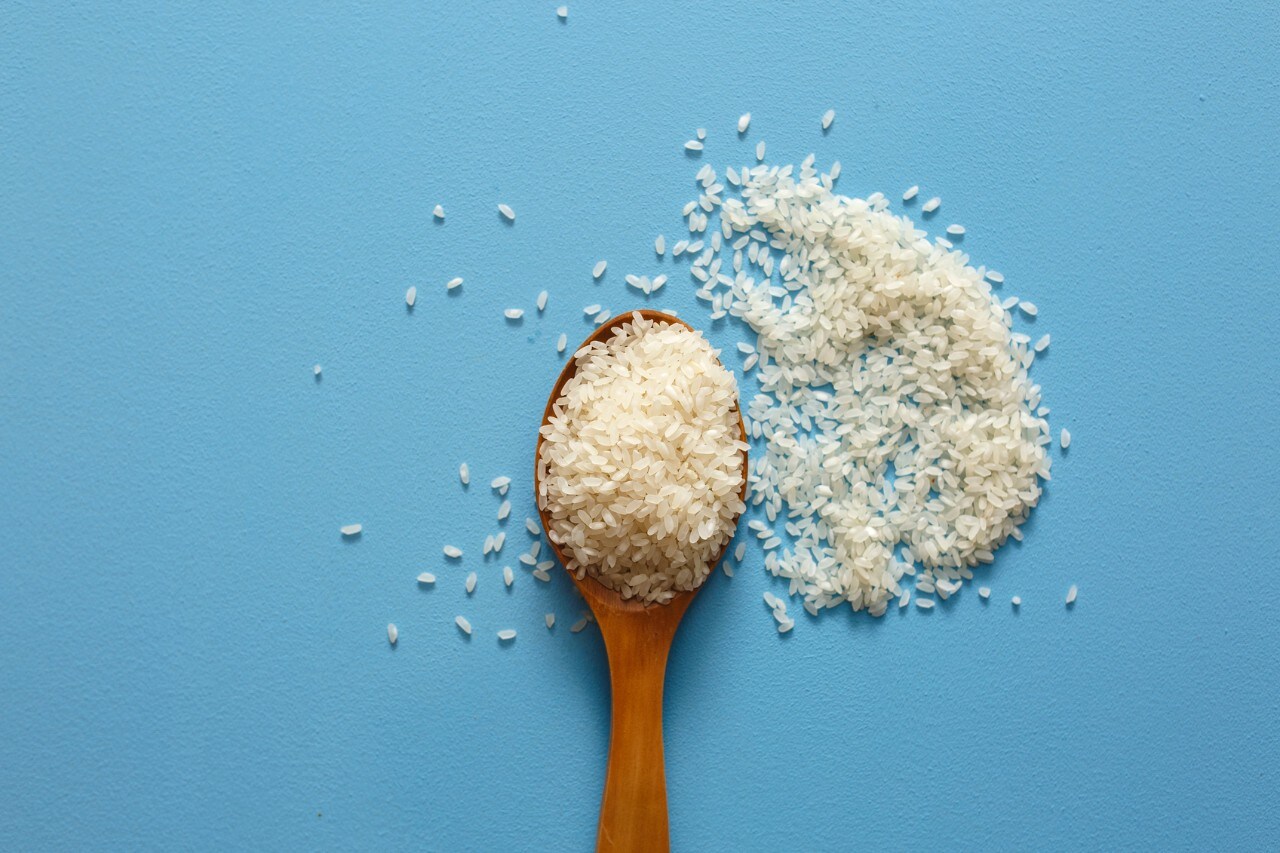 Rice on wooden spoon with blue color background.