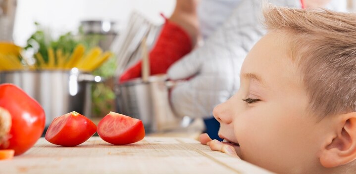 Smiling boy looking at tomato slices on kitchen board