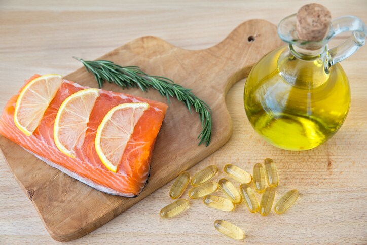 Fish oil capsules, and salmon fillet on wooden surface