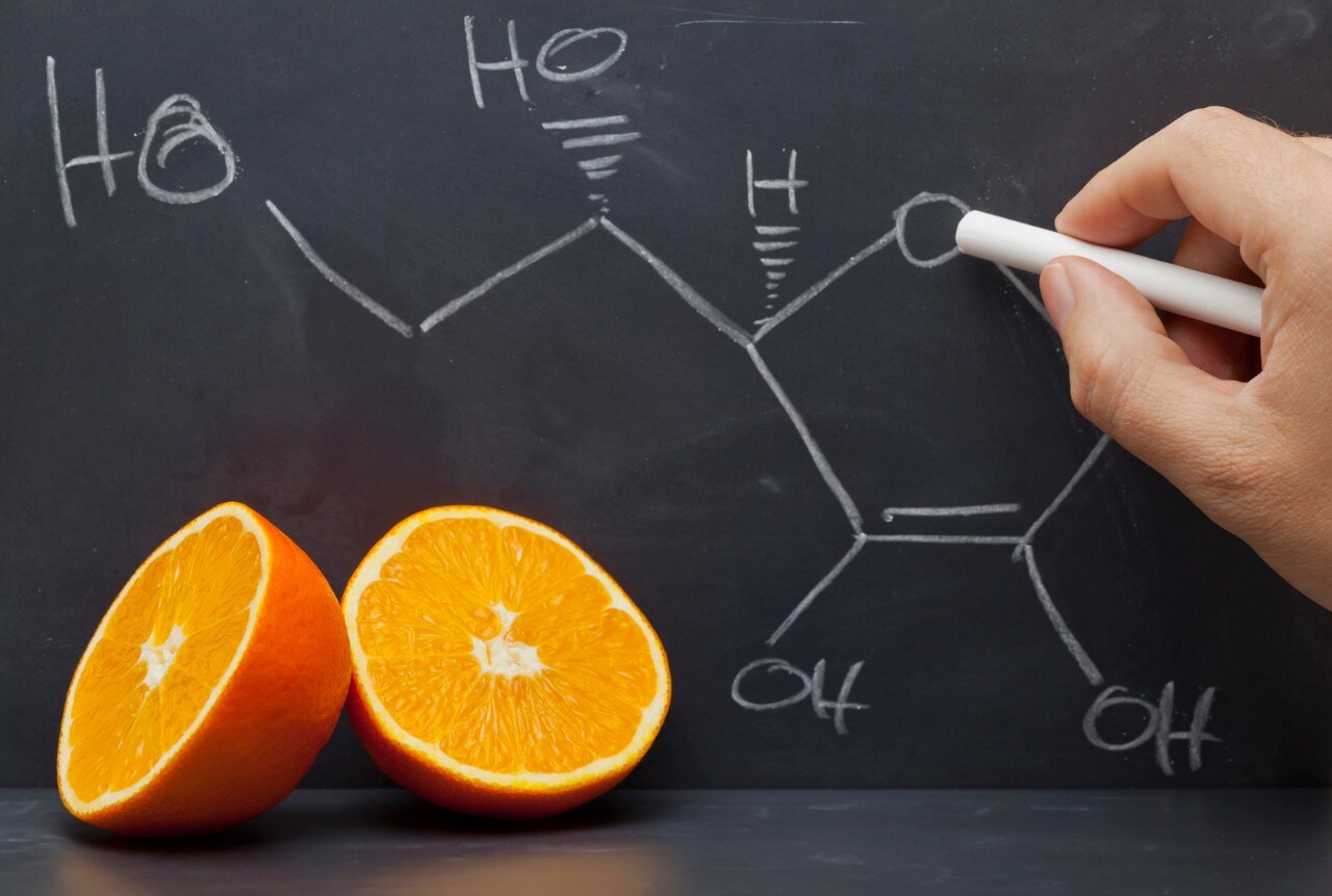 Hand drawing structural formula of vitamin C on blackboard with oranges in front